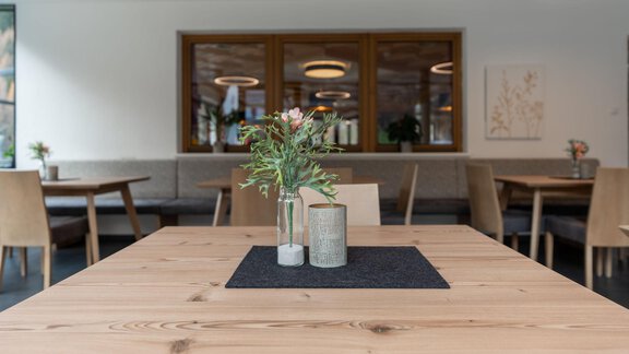 A stylish wooden table with a small vase of flowers and a candle in the center. In the background, cozy seating areas can be seen. - Gasthof Brückenwirt - Zwieselstein