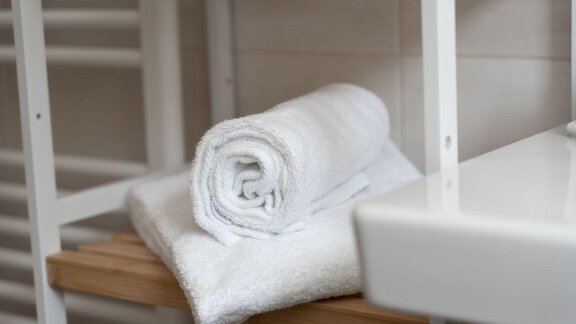 A stack of white towels is neatly arranged on a wooden shelf. The surroundings appear bright and clean. - Gasthof Brückenwirt - Zwieselstein