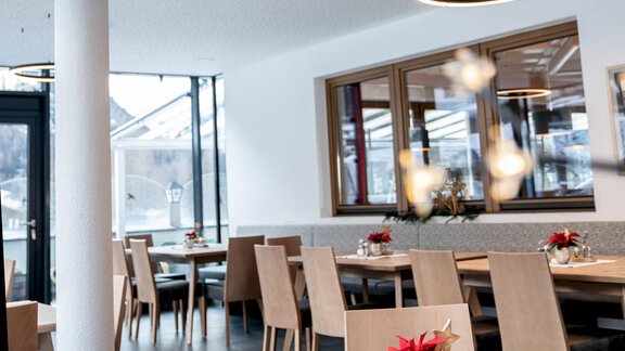 A modern restaurant interior with wooden tables and chairs. Subtle decoration and large windows create an inviting atmosphere. - Gasthof Brückenwirt - Zwieselstein