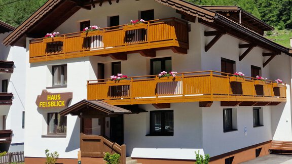 A modern house with balconies and blooming plants. The facade is in white and brown, surrounded by green nature. - Haus Felsblick - Zwieselstein