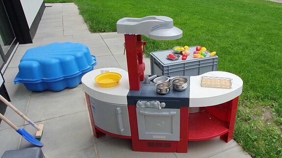 A colorful outdoor play kitchen with cooking utensils and educational toy fruits. In the background, a blue sandbox and green grass can be seen. - Haus Fortuna - Zwieselstein