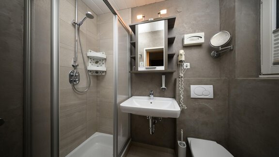 A modern bathroom with a shower, sink, and toilet. The walls are in neutral colors and there is a large mirror. - Haus Sonnschein - Zwieselstein