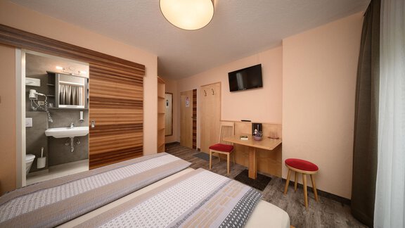 A modern hotel room with two beds and a desk. In the background, there is the bathroom and a television on the wall. - Haus Sonnschein - Zwieselstein