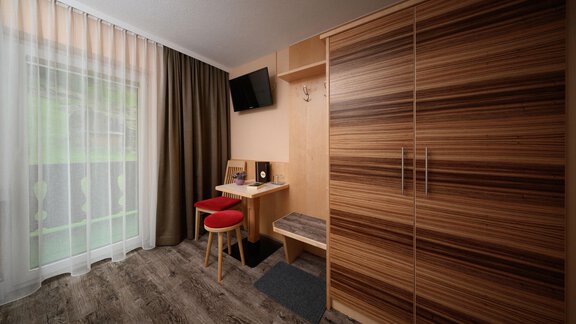 A modern room with a wooden wardrobe, a desk, and a television. Large windows let in a lot of light. - Haus Sonnschein - Zwieselstein