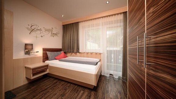 A modern bedroom with a single bed and a large window. The walls are light, and the wooden furniture gives the room a warm atmosphere. - Haus Sonnschein - Zwieselstein