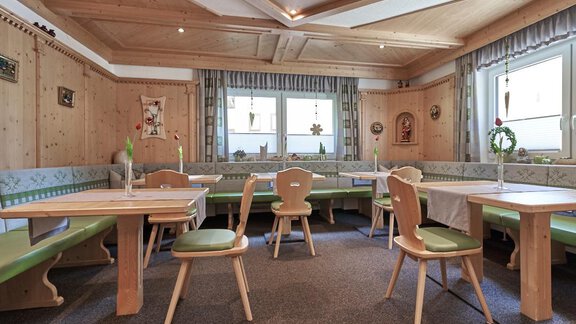 A cozy room with wooden paneling and green benches. There are several tables and windows that let in plenty of light. - Haus Sonnschein - Zwieselstein