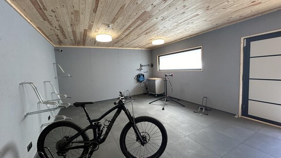 A modern room with gray walls and a wooden ceiling. In the center stands a mountain bike, and wall mounts are installed. - Hochstatt Appartements - Zwieselstein