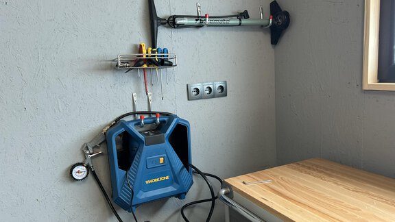 A workspace with a blue device unit on the wall. Next to it, tools and a wooden tabletop are visible. - Hochstatt Appartements - Zwieselstein