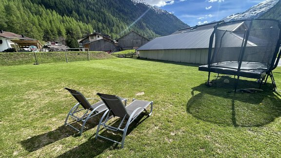 A green garden with two lounge chairs and a trampoline. In the background, there are mountains and a clear blue sky. - Hochstatt Appartements - Zwieselstein
