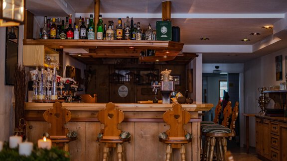 A cozy bar with wooden shelves displaying a selection of drinks. The stools are made of wood and invite you to stay awhile. - Hotel Gasthof Zwieselstein - Zwieselstein