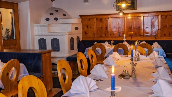 A cozy restaurant with a long table, covered with white tablecloths and folded napkins. In the center, candles burn on elegant holders, and the wooden walls give a rustic charm. - Hotel Gasthof Zwieselstein - Zwieselstein