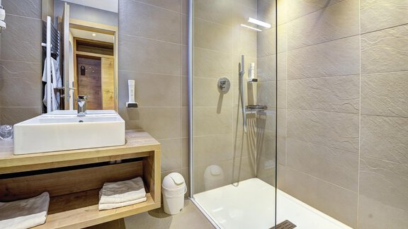 A modern bathroom with a shower and a stylish wooden sink unit. The walls are in neutral colors, creating an elegant atmosphere. - Hotel Neue Post - Zwieselstein