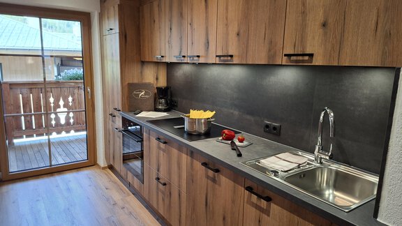 A modern kitchen with wooden cabinets and a large window. - Landhaus Alpenjäger - Zwieselstein