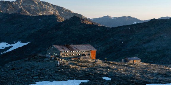 Eine Berghütte liegt zwischen schneebedeckten Flächen und felsigen Hängen. Die Landschaft ist majestätisch und zeigt die ruhige Schönheit der Berge. - Hochstubaihütte - Sölden