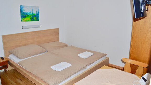 A simple bedroom with a double bed and a table. A picture hangs on the wall and a television is installed. - Haus Maria - Hochsölden