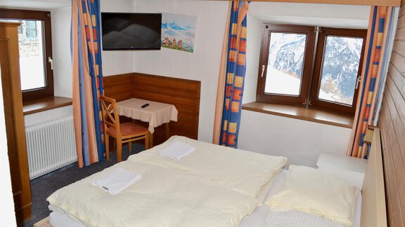 A cozy bedroom with two beds and a table. The room has large windows with a view of the mountains. - Haus Maria - Hochsölden