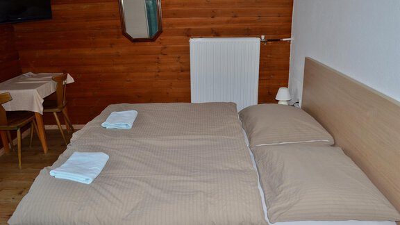 A cozy bedroom with a large bed and beige bedspreads. In the background, there is a table with chairs and a heater on the wall. - Haus Maria - Hochsölden