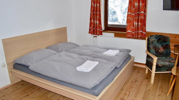A cozy bedroom with a double bed and gray bedding. The room has wooden floors and orange curtains. - Haus Maria - Hochsölden