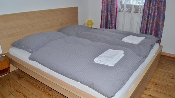 A cozy bedroom with a double bed and gray bed covers. Two folded towels are placed on the bed and a window lets in daylight. - Haus Maria - Hochsölden