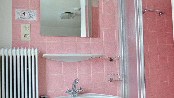 A bright bathroom with pink tiles and a sink. There is a shower cabin and a radiator. - Haus Maria - Hochsölden