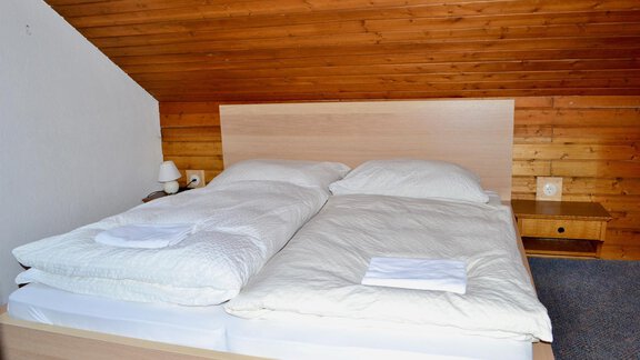 A cozy bedroom with a double bed and bright wood paneling. Fresh bedding is laid on the bed and two nightstands stand beside it. - Haus Maria - Hochsölden