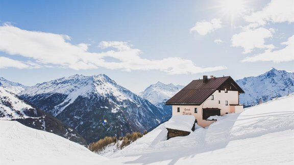 A cozy house sits on a snowy hill with majestic mountains in the background. The sky is clear and sunny, perfect for a winter day in the Alps. - Haus Maria - Hochsölden
