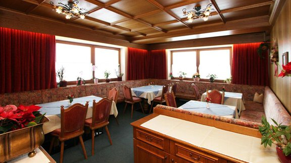 A cozy restaurant with bright windows and elegant tables. The walls are decorated with red curtains and wood-paneled ceilings. - Pension Ferdinand - Hochsölden