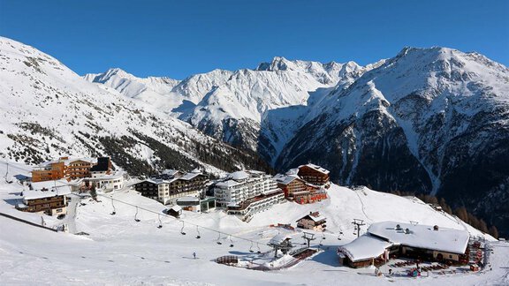 A picturesque mountain landscape with snow-capped peaks and a ski resort in the valley. Cable cars connect the various mountain huts. - Pension Ferdinand - Hochsölden