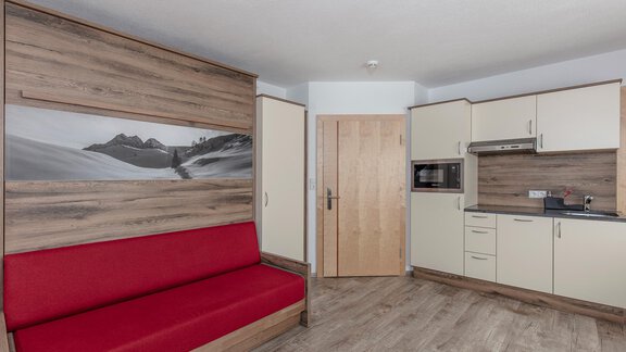 Eine moderne Küche mit einem roten Sofa und holzverkleideten Wänden. Der Raum wirkt gemütlich und gut gestaltet. - Apart Felsenhof - Huben