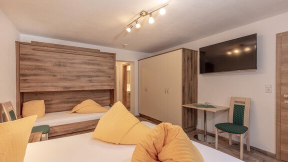 Ein gemütliches Zimmer mit einem Doppelbett und einer Schlafcouch. Es gibt einen Fernseher und einen kleinen Tisch im Raum. - Apart Felsenhof - Huben