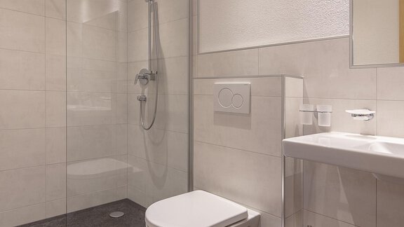 Ein modernes Badezimmer mit einer Duschkabine und einem eleganten Waschbecken. Der Boden ist in dunkler Farbe gehalten und es liegen weiße Handtücher auf dem Boden. - Apart Felsenhof - Huben