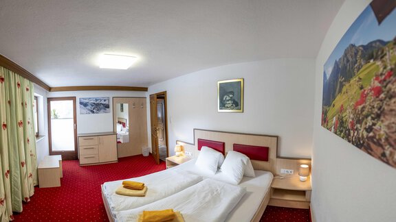 A modern room with a double bed and a cozy sofa. The walls are painted in light colors and a window lets in plenty of daylight. - Berghof Reich - Längenfeld