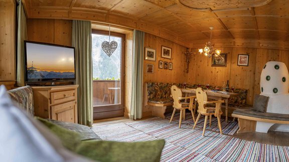 A cozy wooden interior with a sitting area and a table. The walls are decorated with pictures, and a large, white element stands out in the room. - Berghof Reich - Längenfeld