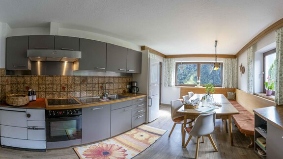 A bright kitchen with a long dining table, lovingly set. The windows allow plenty of daylight in and create a cozy atmosphere. - Berghof Reich - Längenfeld