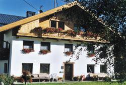 A beautiful house with a wooden gable and flower boxes. In the foreground, there are seating areas and a green garden. - Hauertalerhof - Längenfeld