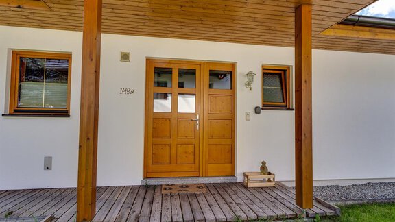 A cozy front door with wooden cladding and a covered entrance. The facade is simple and light, surrounded by a small garden. - Haus Margret - Längenfeld