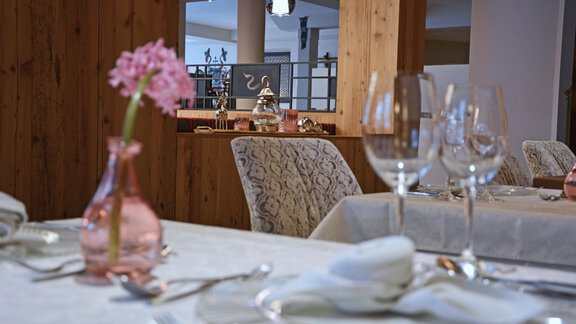 Ein eleganter Esstisch mit Gläsern und Besteck, dekoriert mit einer rosa Blume. Im Hintergrund ist eine gemütliche Restaurantatmosphäre zu sehen. - Hotel Stern - Längenfeld