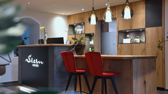 Ein modernes Empfangsbereich mit Holz-Elementen und stilvollen Leuchten. Rote Stühle stehen am Empfangstresen. - Hotel Stern - Längenfeld