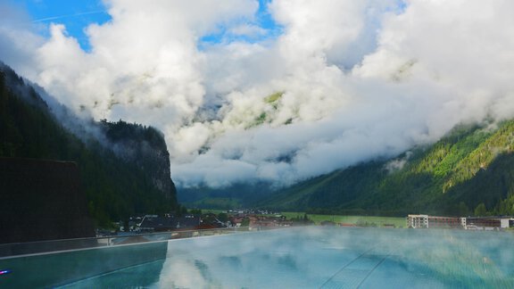 Ein schöner Blick auf ein Infinity-Pool vor einer beeindruckenden Berglandschaft. Die Wolken schweben über den Bergen und reflektieren sich im Wasser. - Hotel Stern - Längenfeld