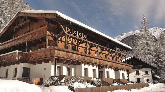 A traditional wooden house in the snow, surrounded by mountains. The sky is blue with some clouds. - Gasthof Stuibenfall - Niederthai