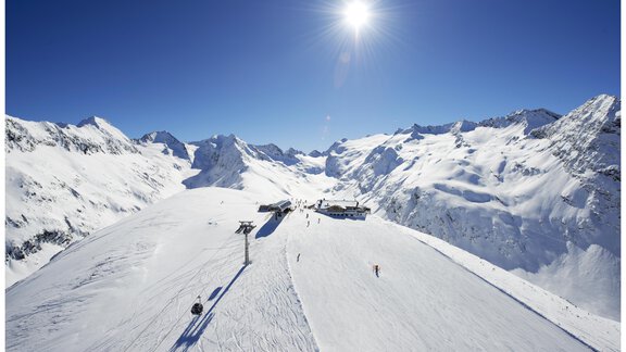 A snow-covered mountain landscape under a blue sky. The sun shines over the majestic mountains and the ski slope. - Ferienwohnung Poschacherhof - Obergurgl 