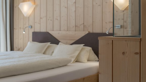 A cozy bedroom with a wooden wall design and a large bed. The soft lighting creates a relaxing atmosphere. - Hotel-Garni Pirchhütt - Obergurgl 