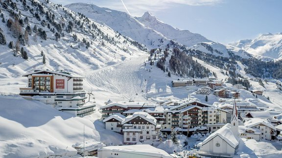 A picturesque winter village, surrounded by snow-covered mountains. The buildings and slopes are hidden under a white blanket of snow. - Hotel Gotthard-Zeit - Obergurgl 