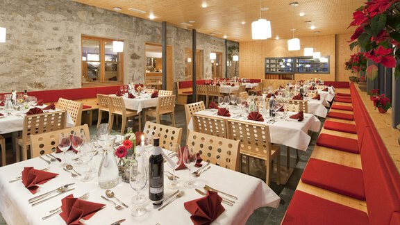 An elegant table in a restaurant, set with glassware and red cutlery. In the background, large windows and a cozy atmosphere are visible. - Universitätszentrum Obergurgl - Obergurgl 