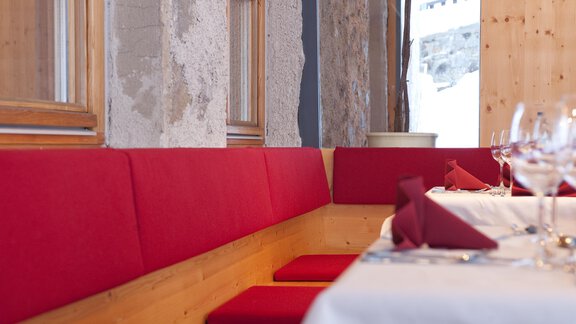 A cozy dining area with red seat cushions and a festively set table. The walls are made of wood and stone, creating a warm atmosphere. - Universitätszentrum Obergurgl - Obergurgl 