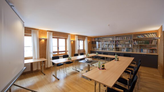 A modern meeting room with a long table and chairs. Shelves filled with books line the walls, and large windows let in plenty of light. - Universitätszentrum Obergurgl - Obergurgl 