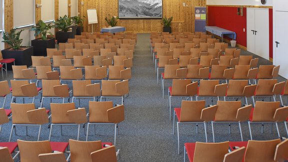 A large, empty conference room with many orange chairs. In the background, a screen is visible with an image. - Universitätszentrum Obergurgl - Obergurgl 
