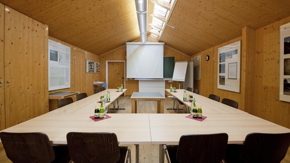 A bright meeting room with wooden walls and large windows. In the center stands a large table with chairs and presentation technology. - Universitätszentrum Obergurgl - Obergurgl 