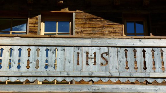 A traditional wooden house with a balcony railing. The letters "IHS" are artistically incorporated. - DreiHäuser - Obergurgl 