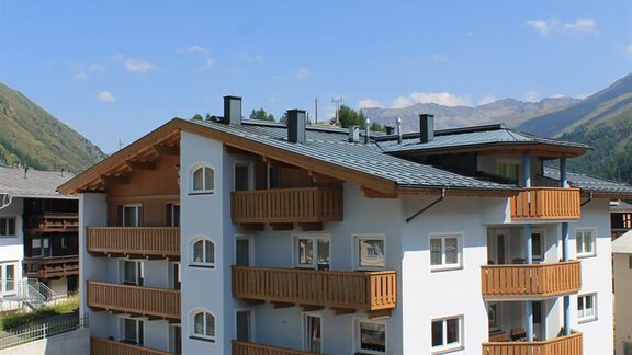 A modern building with white walls and wooden balconies. In the background, green mountains and a blue sky can be seen. - Haus Martinshof - Obergurgl 
